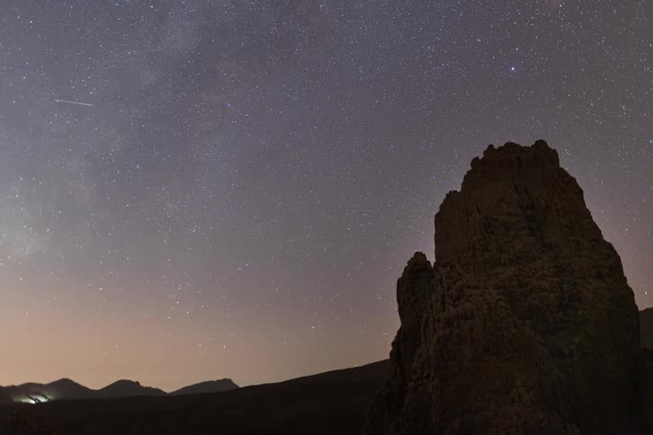 A stunning timelapse shows a meteor shower and the Milky Way galaxy moving across the night sky above a silhouetted rock formation in the desert