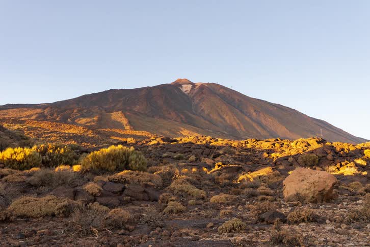 A golden hour timelapse shows the sun setting over the El Teide volcano, casting long shadows across the arid, rocky landscape of Tenerife
