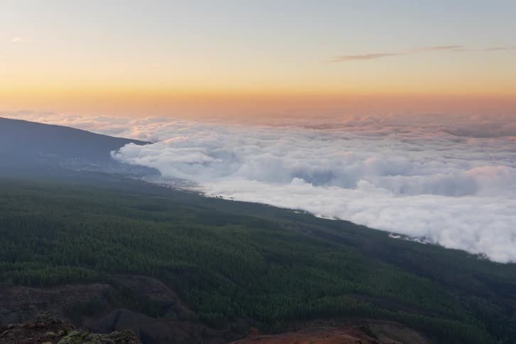 A stunning timelapse captures a sea of clouds flowing over a mountain forest as the sun sets, painting the sky in warm hues