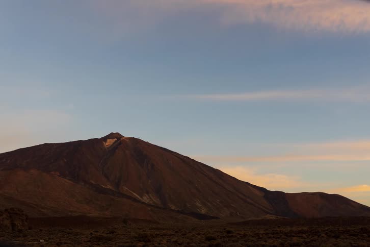 A time-lapse captures a colorful sunrise over the majestic Teide volcano in Tenerife, with pink clouds fading as the morning light illuminates the peak
