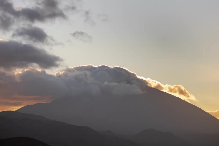 A majestic time-lapse captures clouds swirling over a silhouetted mountain during a beautiful golden hour sunset
