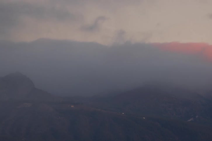 A serene timelapse shows thick fog lifting from a mountain range, revealing the peaks as they catch the warm, golden light of sunrise