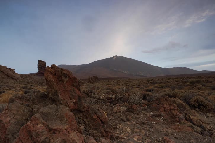 A slow dolly time-lapse reveals the majestic Mount Teide volcano at sunrise, with clouds moving across the sky over a vast, rocky, and arid landscape