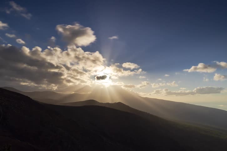A timelapse captures the sun setting behind a mountain range as clouds drift by, creating dramatic sun rays
