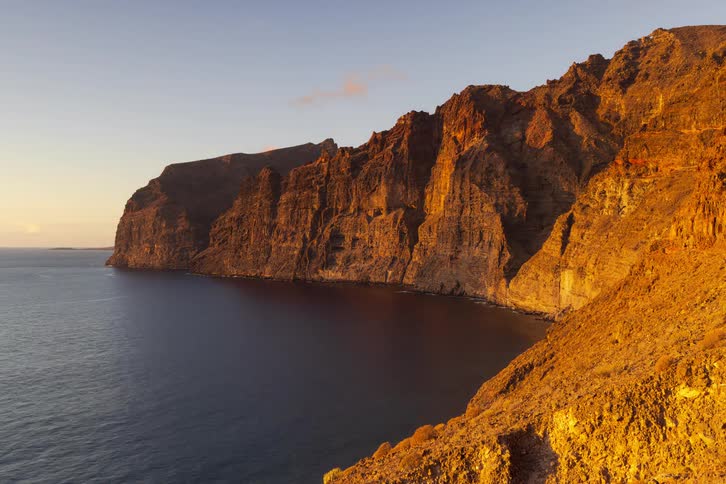 A timelapse of the sun setting over the majestic Los Gigantes cliffs in Tenerife, casting a warm golden light before fading into twilight
