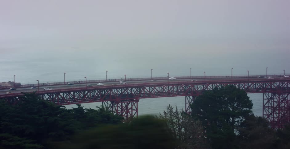 Driving past the iconic Golden Gate Bridge on a foggy day as traffic crosses and a cargo ship sails in the bay