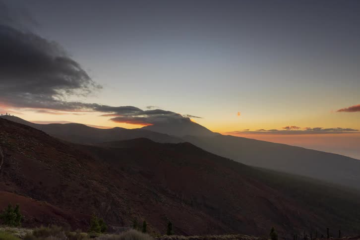 An epic time-lapse of the sun setting behind a majestic mountain, as clouds drift by and the sky transitions from day through a colorful twilight into night
