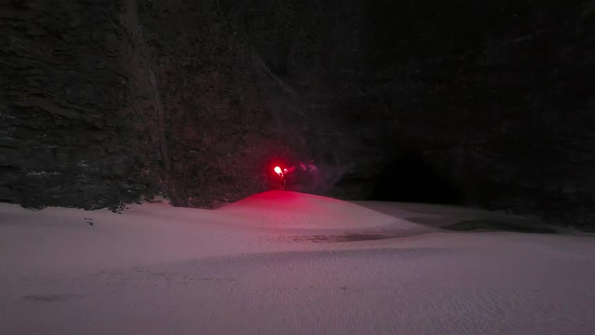 A person standing on a snowy hills top holding a flare in the dark