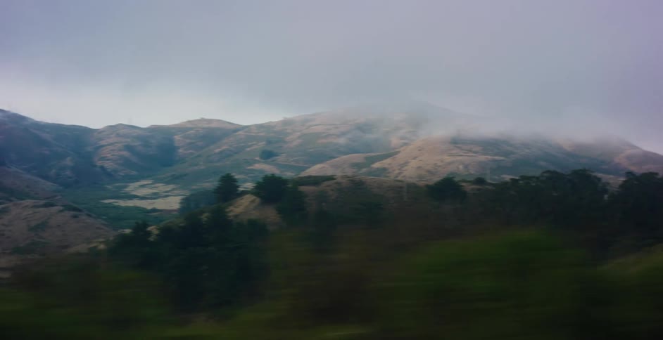 A scenic view from a moving vehicle captures a vast, misty mountain range on an overcast day