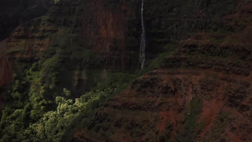 A waterfall trickles down the side of a new red cliffside covered and trees in bush's