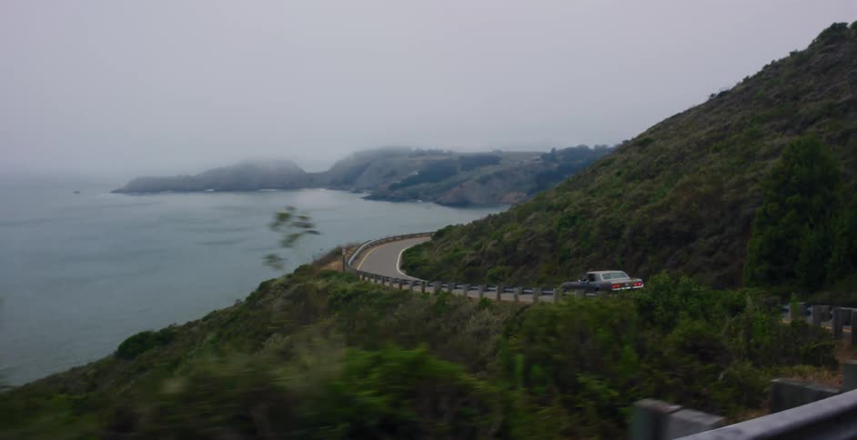 POV shot following a vintage car driving along a winding coastal highway overlooking the foggy ocean