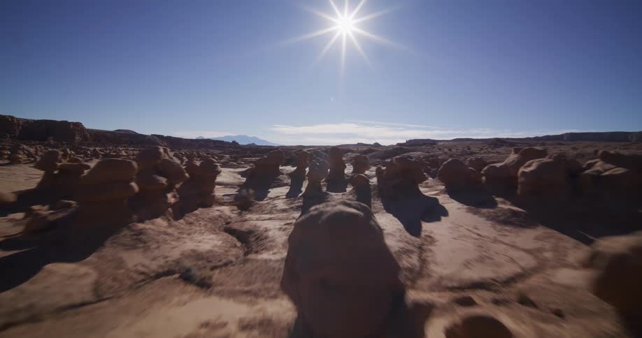 An epic aerial tracking shot moves through the unique rock formations of a desert valley under a bright sun