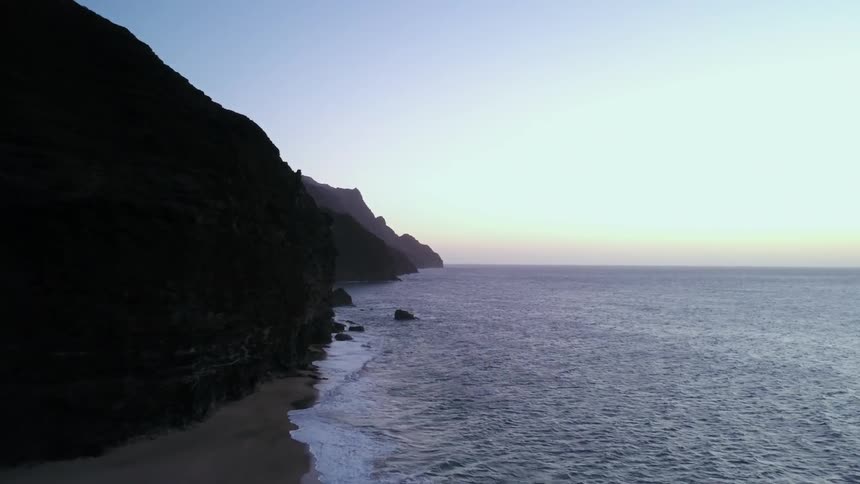 The waves roll onto a beach and the base of steep cliffs