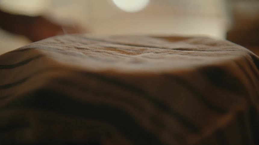 A striped kitchen towel is placed over a bowl of bread dough, letting it proof in a warm, cozy kitchen