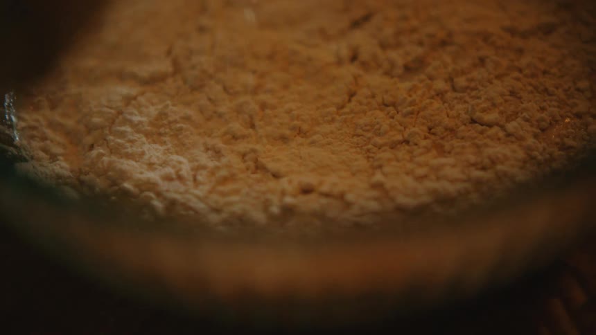 A close-up shot of flour being added to a wet mixture in a glass bowl during the baking process
