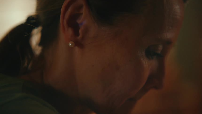 An intimate close-up of a solemn woman's profile, lost in thought under soft, warm light
