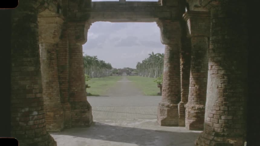 A vintage film view from inside a weathered brick building reveals a long, symmetrical path lined with majestic palm trees