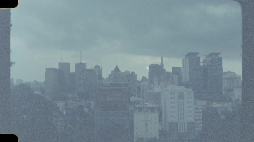 Grainy and atmospheric vintage 8mm footage of a city skyline on a cloudy day