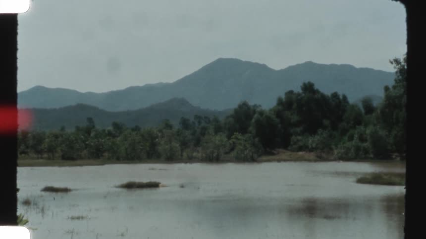 Vintage Super 8 footage captures a serene and hazy mountain landscape with a lake in the foreground