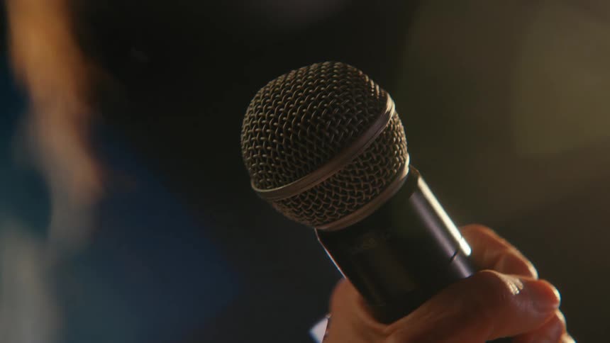 A dramatic close-up of a hand grabbing a microphone on a dark stage