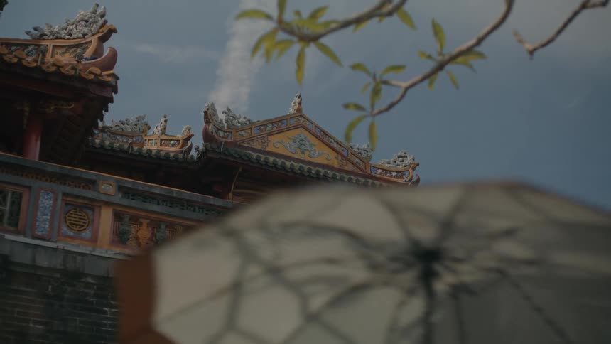 A traditional paper umbrella passes in front of an ornate Asian temple roof under a clear blue sky