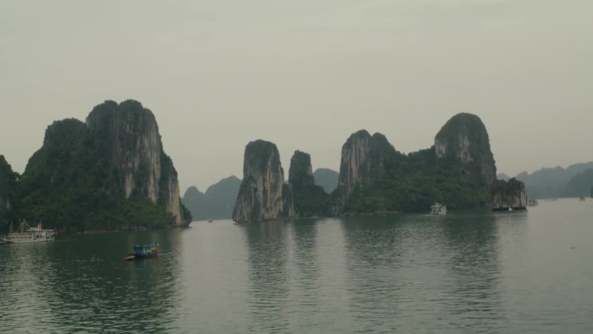 Majestic limestone islands rise from the calm waters of Ha Long Bay in Vietnam on an overcast day