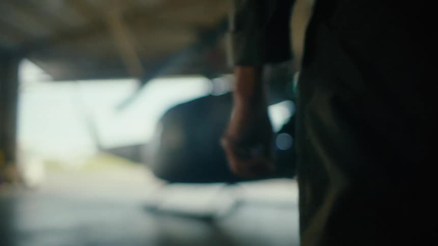 Dramatic close-up of a nervous pilot's hand as they slowly walk towards a helicopter in a hangar