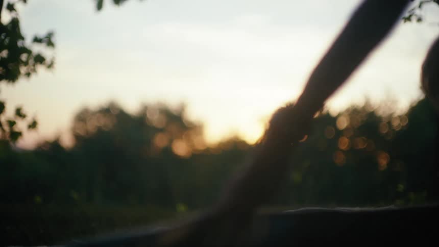 A silhouetted person lays out a picnic blanket in slow motion on a grassy field during a warm sunset