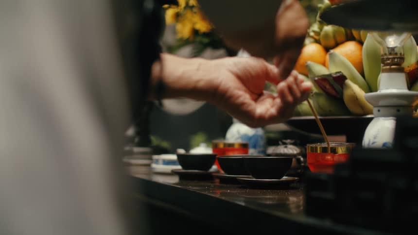 Close-up of a person's hands carefully pouring a thin stream of liquid into a ceremonial cup on an altar