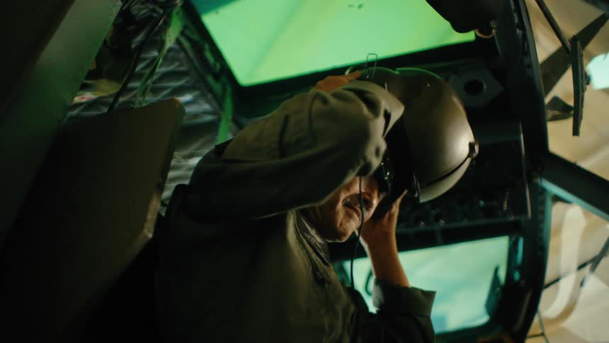 An elderly pilot puts on a helmet and gets ready for flight in the cockpit of a military helicopter