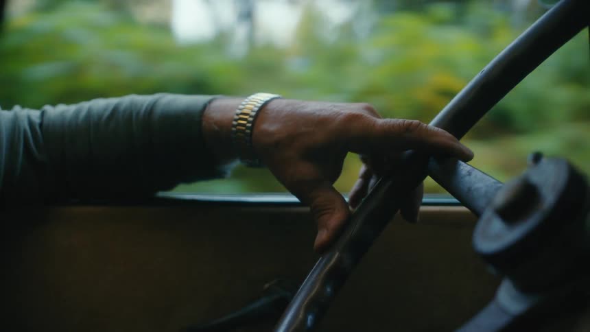 Close-up of a person's hand on a vintage steering wheel during a scenic drive through the countryside