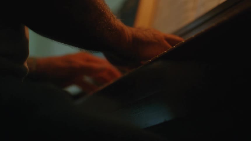 An intimate close-up shot of a man's hands gracefully playing the piano in a dimly lit room