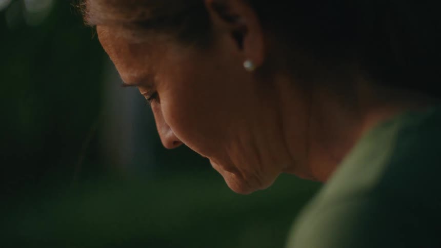 Close-up profile of a somber senior woman looking down in quiet contemplation at dusk