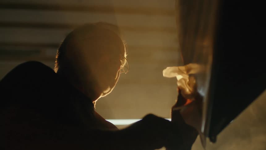 A backlit craftsman meticulously polishes a surface in his dusty, sun-drenched workshop