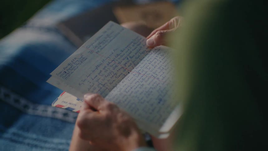 An over-the-shoulder shot captures hands carefully reading a vintage handwritten letter, evoking nostalgia and memories