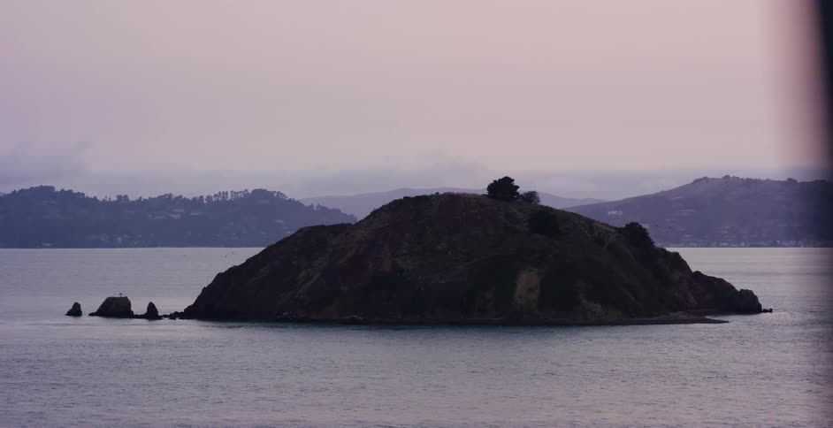A scenic parallax view of a lone island in the bay from a bridge on a moody, overcast day