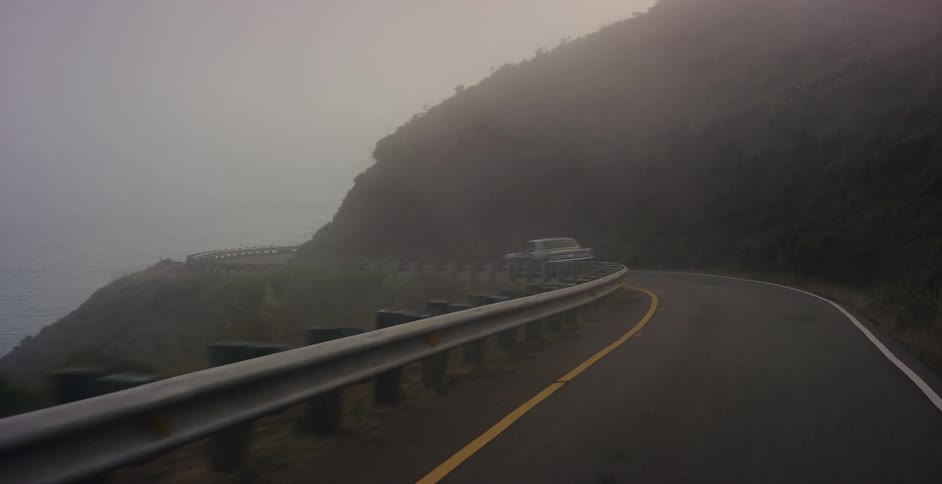 Following a classic muscle car as it drives down a moody, foggy coastal highway