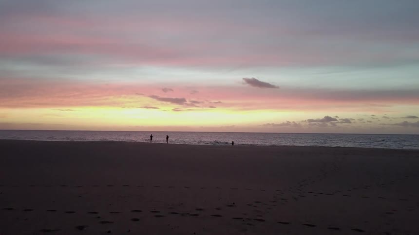 People play on the beach at sunset