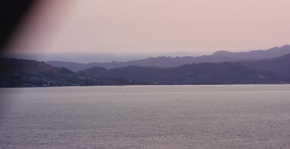 A serene point-of-view shot moving across a bridge, revealing a view of a tranquil bay and hazy mountains at dusk