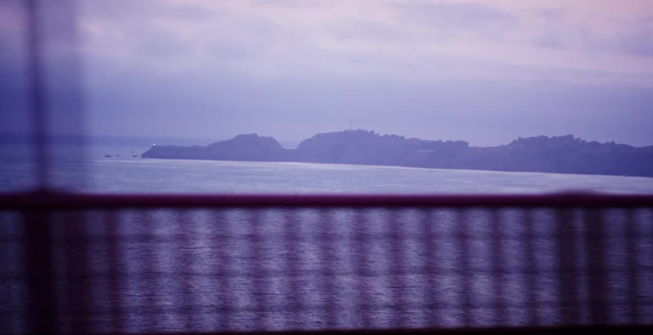 A dreamy point-of-view shot driving across the Golden Gate Bridge looking out at the foggy coastline at dusk