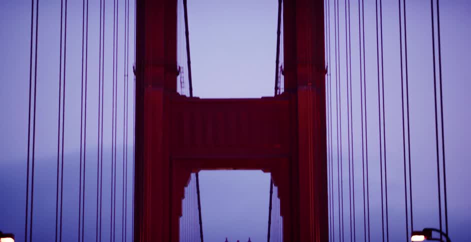 A dramatic tilt down shot from the iconic towers of the Golden Gate Bridge to the illuminated roadway with traffic at twilight