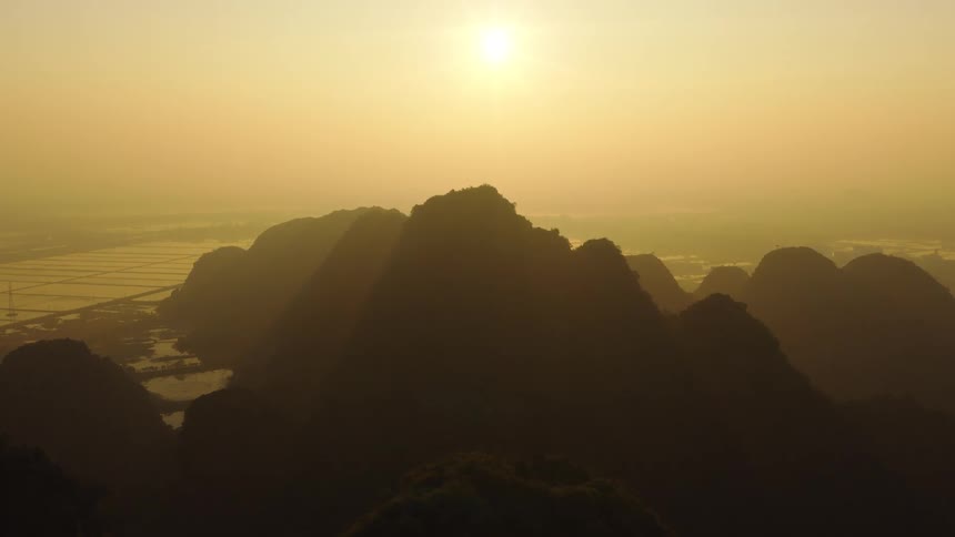 An aerial view slowly pulls back to reveal a stunning mountain range silhouetted against a hazy golden sunrise over a vast valley