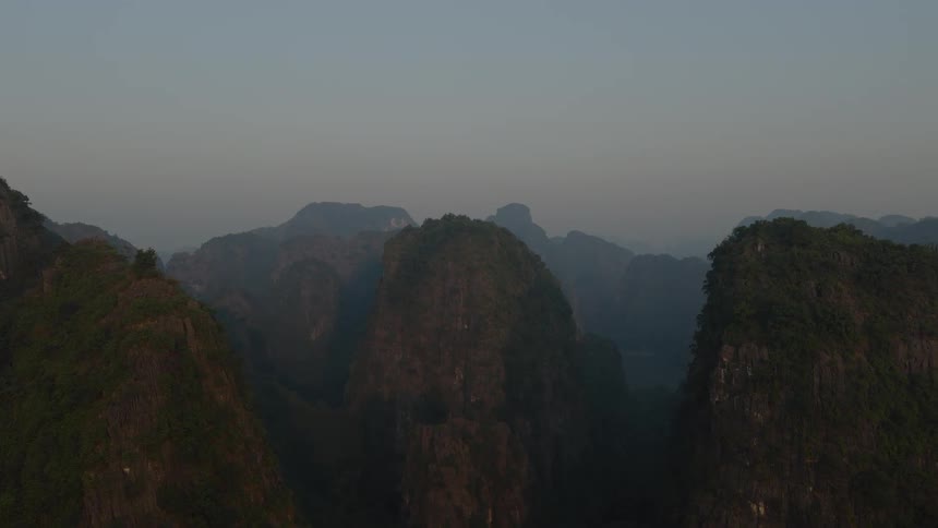 An epic aerial view slowly reveals a vast, hazy landscape of lush green mountains at sunrise