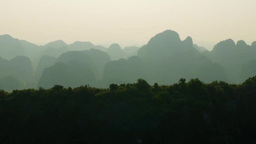 Hazy sunrise illuminates layers of lush green mountains receding into the distance