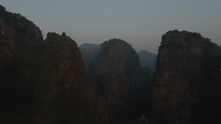 A slow aerial zoom out reveals the majestic, lush mountain peaks of a quiet valley at dusk