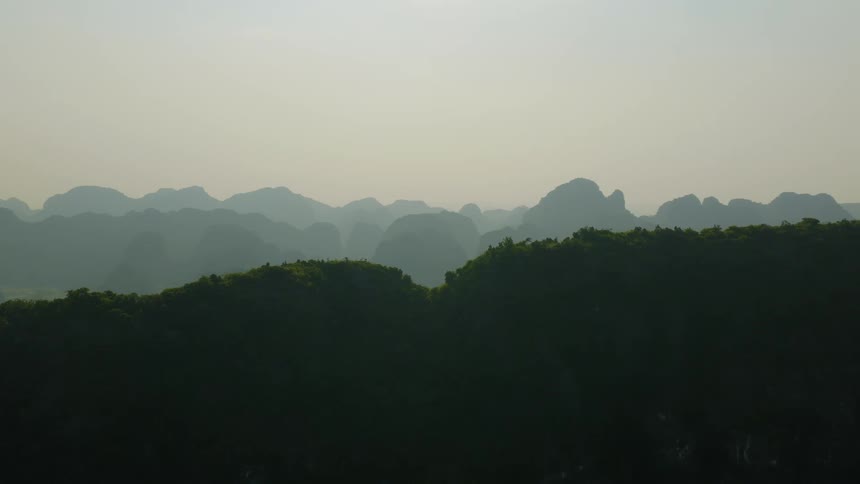 Lush, green mountain ranges are layered into the distance under a hazy, bright sky