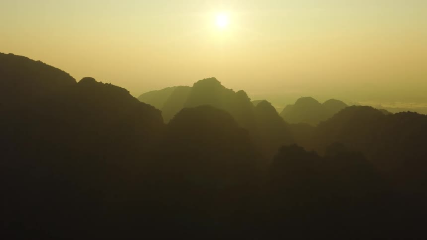 The sun rises over a vast, hazy mountain range, casting the peaks in a stunning silhouette