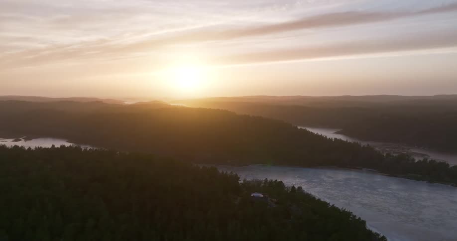 A stunning aerial view captures the golden sunset over a vast landscape of forested hills and a tranquil, misty lake