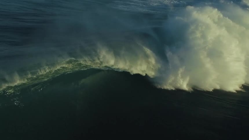 A powerful, sunlit ocean wave forms a perfect barrel as it breaks in dramatic slow motion