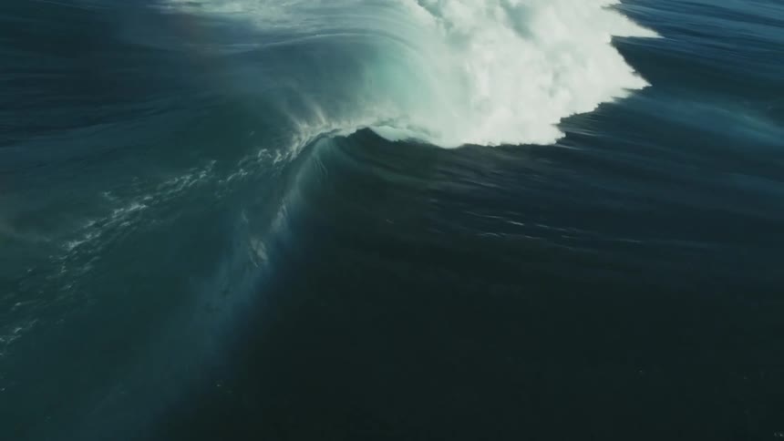 A single, massive ocean wave builds and breaks in dramatic slow motion, revealing a rainbow in its misty spray as it crashes